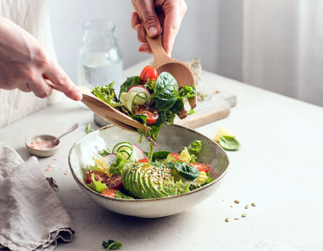Hands mixing a fresh vegetable salad with a wooden spoon in a ceramic bowl, healthy eating and home cooking concept with copy space