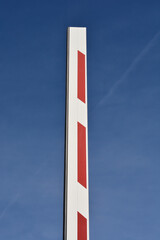 A raised red and white striped parking barrier boom gate arm pointing upwards against a clear blue sky © nahhan