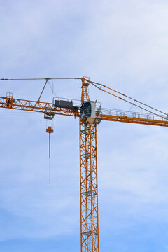 A large yellow construction tower crane with a operator cabin standing high against a bright cloudy sky