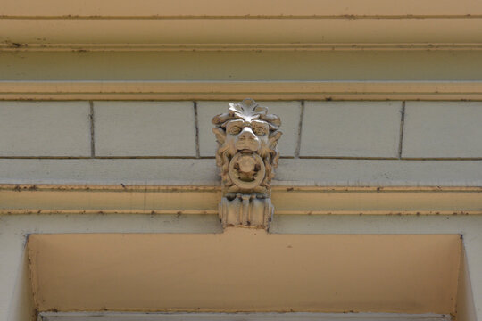 A detailed stone carving of a mythical grotesque face serving as an ornate keystone element over a classic window frame