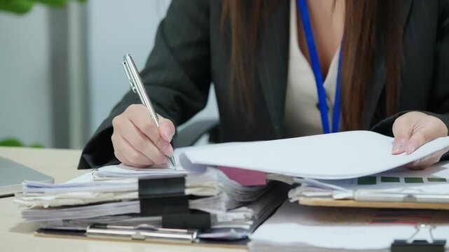 Businesswoman Reviewing Paper Documents and Taking Notes at Office Desk