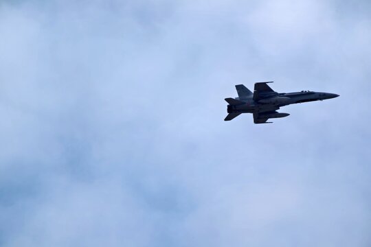 A fighter jet is soaring through the cloudy sky, showcasing its aerodynamic design and military capabilities. The aircraft is seen in flight against the backdrop of soft clouds.