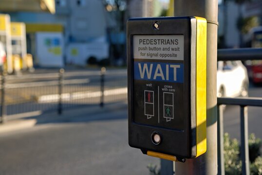 A close up view of a pedestrian push button control box on a metal pole for crossing a street with instructions to wait for the signal