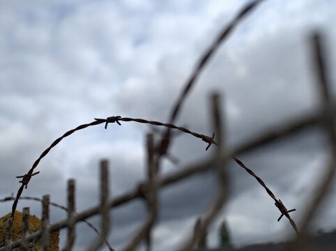 Rusty barbed wire fence showing security and boundary lines under a grey cloudy sky