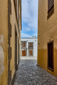 Traditional Canarian architecture featuring a stone-paved street, yellow building facades, and wooden windows near Casa de Colon in Vegueta.