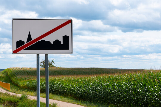 Road sign marking the end of a built-up area beside a rural road, corn field and bicycle path in a sunny countryside landscape