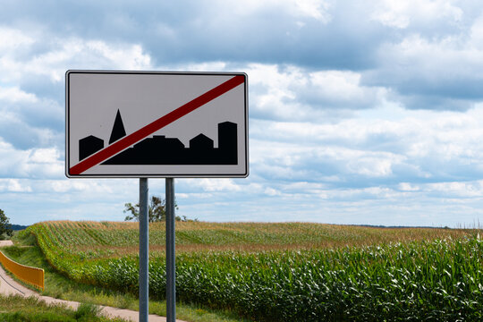 Road sign marking the end of a built-up area beside a rural road, corn field and bicycle path in a sunny countryside landscape