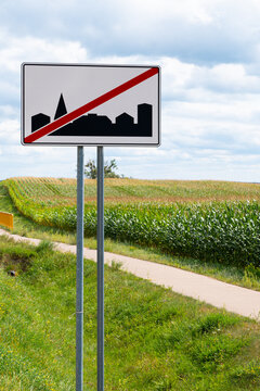 Road sign marking the end of a built-up area beside a rural road, corn field and bicycle path in a sunny countryside landscape