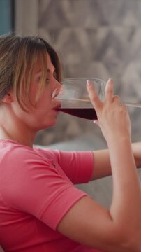 Close up of woman drinking red wine from glass while wearing pink shirt. scene shows texture detail of her clothing and hand with soft lighting in indoor setting featuring patterned