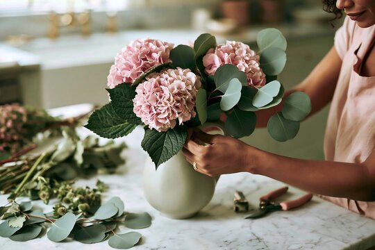 Florist arranging pink hydrangea and eucalyptus bouquet in vase on marble table
