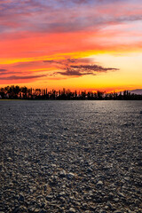 Naklejka premium A vast gravel field and silhouetted trees under a vibrant sunset sky