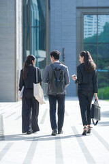 A group of three smartly dressed coworkers striding away down a shaded colonnade in a covered...