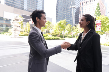 Fototapeta premium A male and female executive meeting outdoors closing a negotiation with a handshake against a backdrop of modern skyscrapers, an authentic look at working life in a busy business district