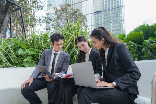 Three multiethnic business colleagues comparing a printed report against a laptop screen among tropical planting outside the office, showing how business happens beyond the meeting room