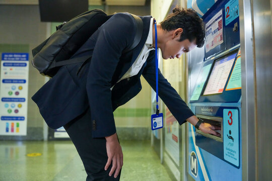 A confident male professional in a suit choosing a fare on a touchscreen ticket machine in a modern subway station on the way to work, reflecting the routine of urban working life