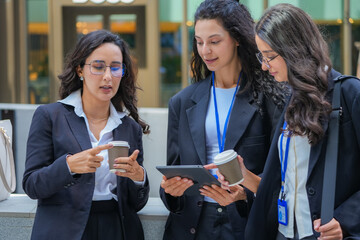 Obraz premium A team of three Hispanic businesswomen in matching dark suits, one making an emphatic point with her hand, discuss a session over coffee at a business event, in the business district.