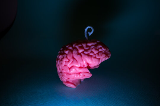 Handmade pink sculptural candle shaped like a human brain with a wick on top. Dramatic neon lighting creates a creepy Halloween atmosphere for horror decor, spooky parties and unusual interior decorat