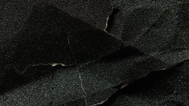 Torn Black Surface Texture. Macro view of rough dark material with irregular tears, broken edges and subtle camera movement.