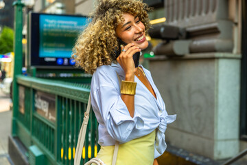Fototapeta premium Happy woman talking on phone near new york subway entrance