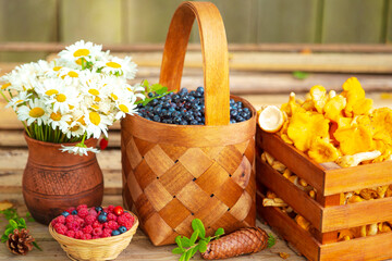 Ripe juicy blueberries in a wicker basket, raspberries, chanterelles in a wooden crate  and chamomile flowers. © lizavetta