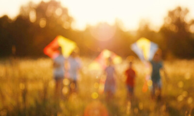 Naklejka premium A blurred image of children playing in a field during sunset, joyfully flying colorful kites. The warm light creates a cheerful and nostalgic atmosphere.