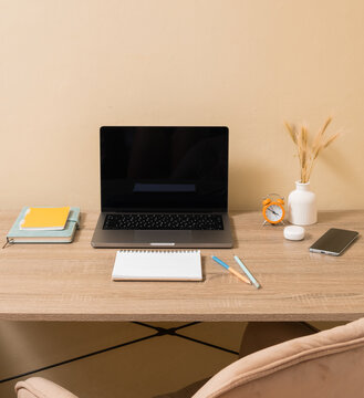Home office setup with laptop and stationery on a wooden desk in a simple room