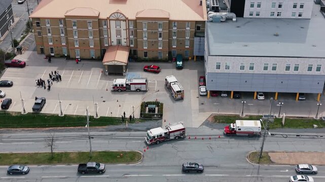Aerial view captures the urgency as fire trucks gather outside a hotel in Halifax, Nova Scotia. Evacuated individuals stand on the street, witnessing the unfolding situation