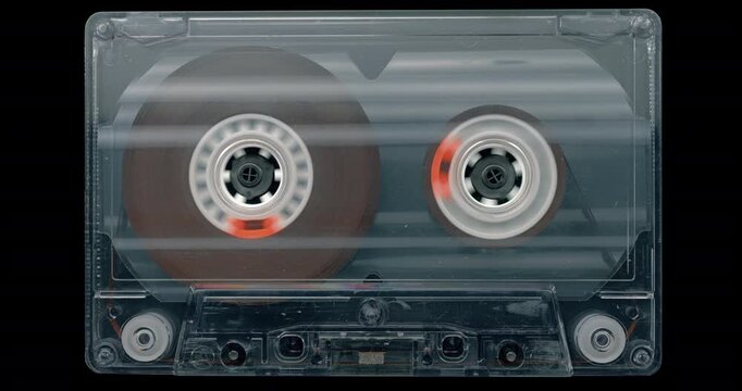 Fast Rewinding Audio Cassette. Transparent cassette with rapidly spinning reels and magnetic tape moving during fast rewind on black background. 