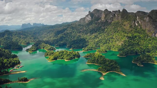 Cheow Lan Lake in Khao Sok National Park, Thailand, numerous jungle covered limestone karst islands and mountains rising from emerald green water under a cloudy sky. Amazing nature aerial landscape