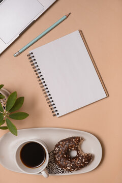 A workspace with a notebook, coffee, a donut, and a plant on a table