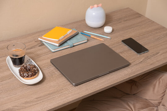 Working space with laptop, coffee, snacks, and stationery on wooden desk