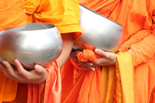 Close-up of Buddhist monks holding alms bowls in traditional orange robes.