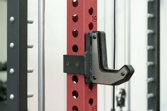 Close-up of a J-hook attachment mounted on a smith machine in a gym, designed to support a barbell during strength training and weightlifting exercises.