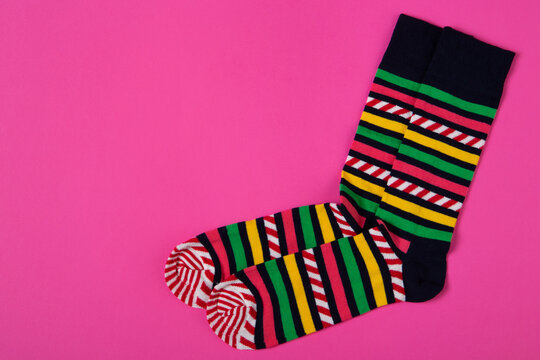 Pair of colorful striped socks on pink background with copy space. Bright casual knit hosiery flat lay top view