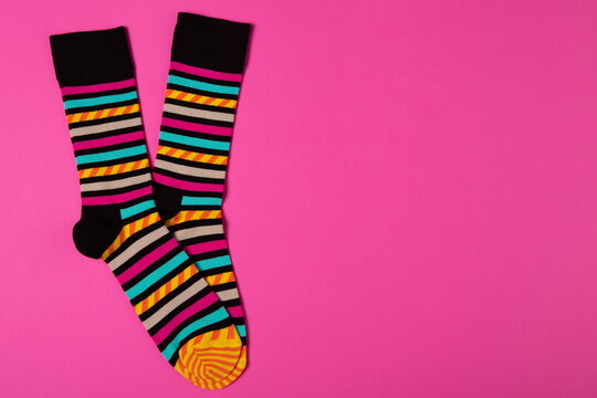 Pair of bright striped socks on pink background with copy space. Trendy multicolored casual socks flat lay top view