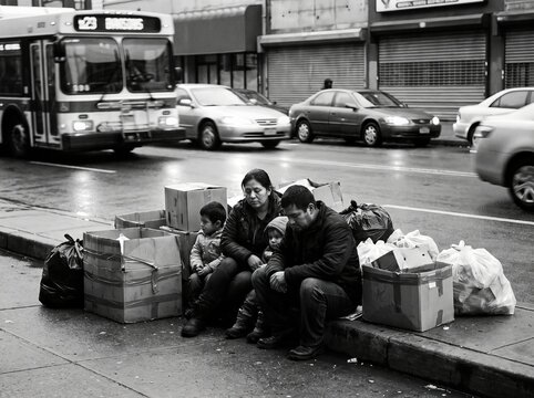 Sad family sitting on street curb next to packed cardboard boxes