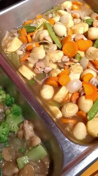 Vertical pan shot of Asian buffet catering featuring chicken broccoli and mixed vegetable stir-fry in chafing dishes