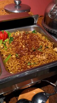 Vertical pan of Indonesian catering buffet featuring fried noodles, spicy stir fry, and meatball soup station