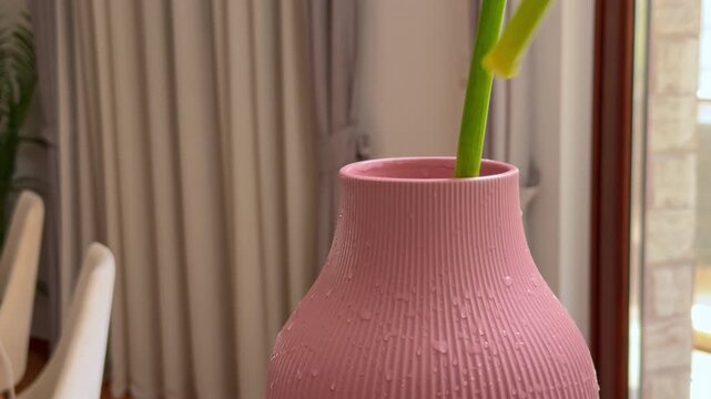Green plant stems are placed and arranged inside a textured pink ceramic vase on a table indoors, a simple home decor styling moment.