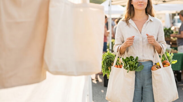 Woman carrying reusable shopping bags filled with fresh vegetables at a farmer market