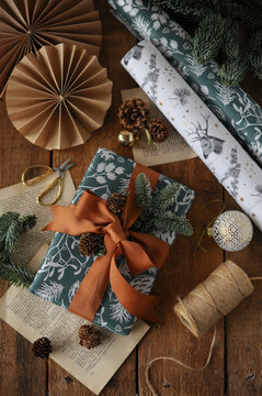 Cozy Christmas gift wrapping flat lay with rustic decorations, vintage paper, ribbon, pine cones, and festive wrapping paper on wooden background