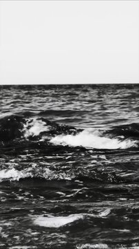 A serene black and white landscape of the ocean with waves and misty atmosphere