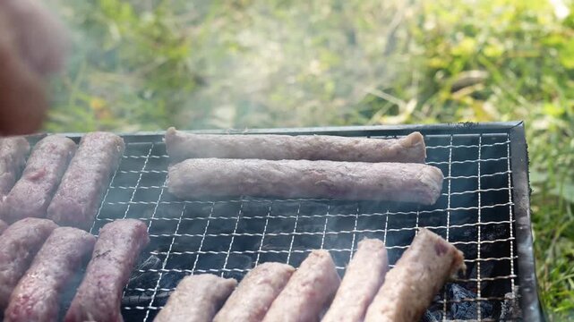 Male hand places cevapi on a charcoal grill with rising smoke outdoors. Traditional barbecue footage fits food, travel, summer and hospitality themes
