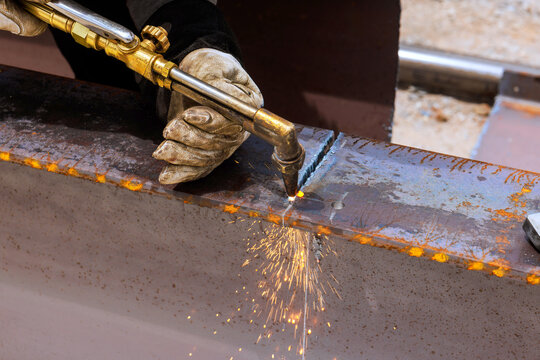 Worker uses torch to weld two pieces of metal together in workshop sparks fly as metal heats up.