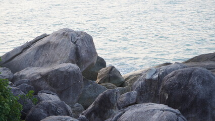 Large, rounded granite boulders stacked along a shore overlooking a calm sea. © Ahmad