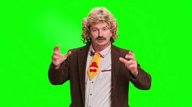 An adult man wearing a curly blonde wig, fake mustache and brown jacket turns and gestures while speaking against a green screen background, a comedic retro character concept with copy space.
