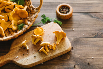 Fototapeta premium Fresh chanterelle mushrooms on a wooden board and in a basket on a dark table, rustic harvest scene, healthy cooking ingredients, organic forest food, autumn season. Top view, flat lay, copy space.