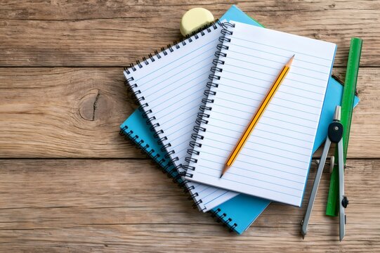 School supplies with notebooks, pencil, and compass on wood background