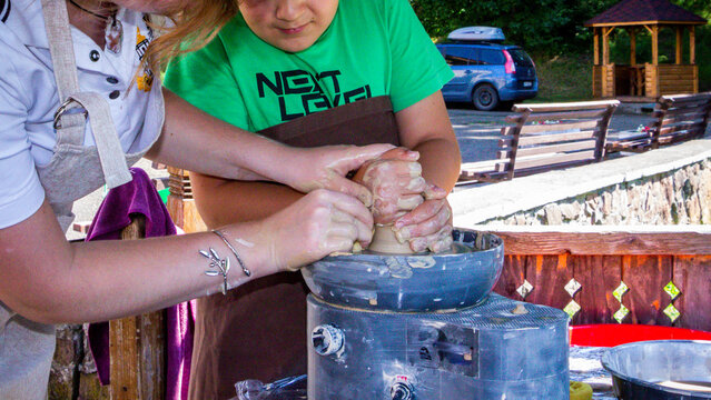 woman teaches teenager pottery, clay modeling, centering and pulling the walls of future pottery by hand, master