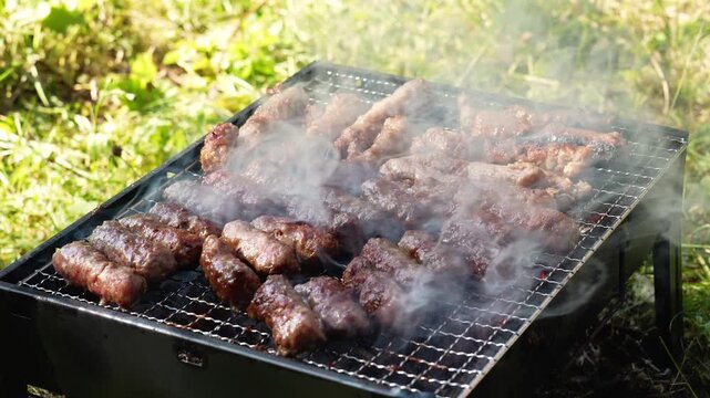 Cevapi cook on a hot charcoal grill as thick smoke rises outdoors. Traditional Balkan barbecue footage fits food, travel, summer and hospitality themes